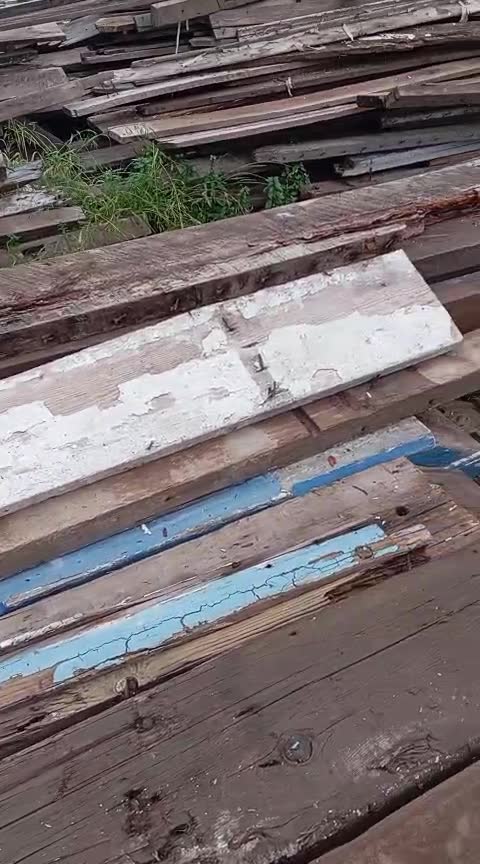 Tablones con restos de pintura blanca y clavos, apilados en el patio del taller