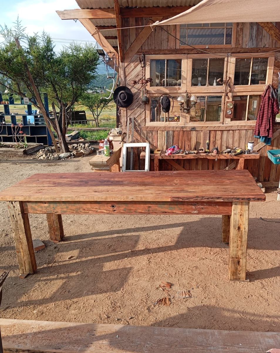 Mesa de tablón de roble terminada, con su banca, en el patio del galpón y el cerro de fondo